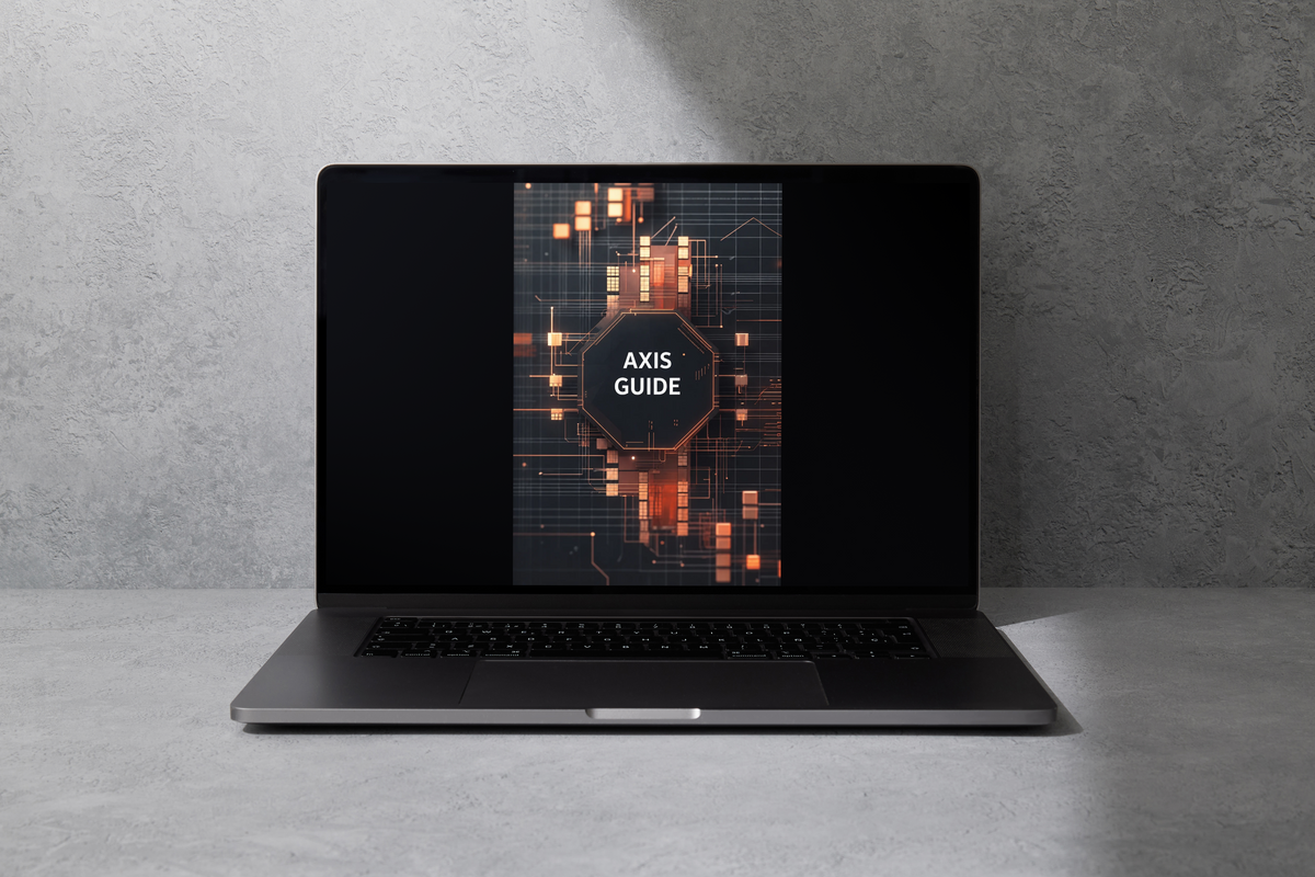 A dark gray laptop sits open on a light gray concrete surface against a textured gray wall. The screen displays a digital cover titled 'AXIS GUIDE' with a glowing orange and black circuit board graphic.