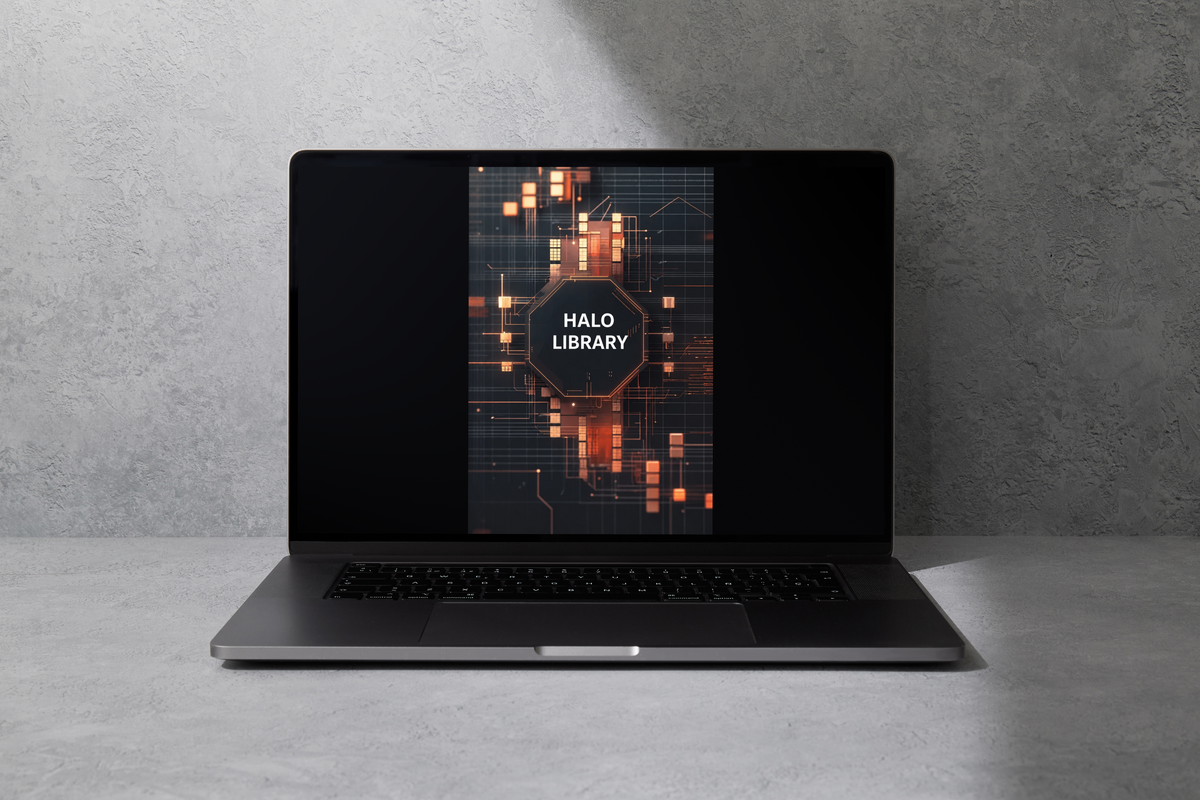 A dark gray laptop sits open on a light gray textured surface against a matching gray wall. The screen displays a digital cover for 'HALO LIBRARY' with a glowing orange and black circuit design.